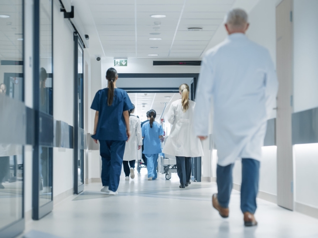 Hospital Hallway with Doctors, Nurses and Specialists in Hospital. Female and Male Physicians, Surgeons, Healthcare Officials Walk Together in Corridor with Their Back to Camera