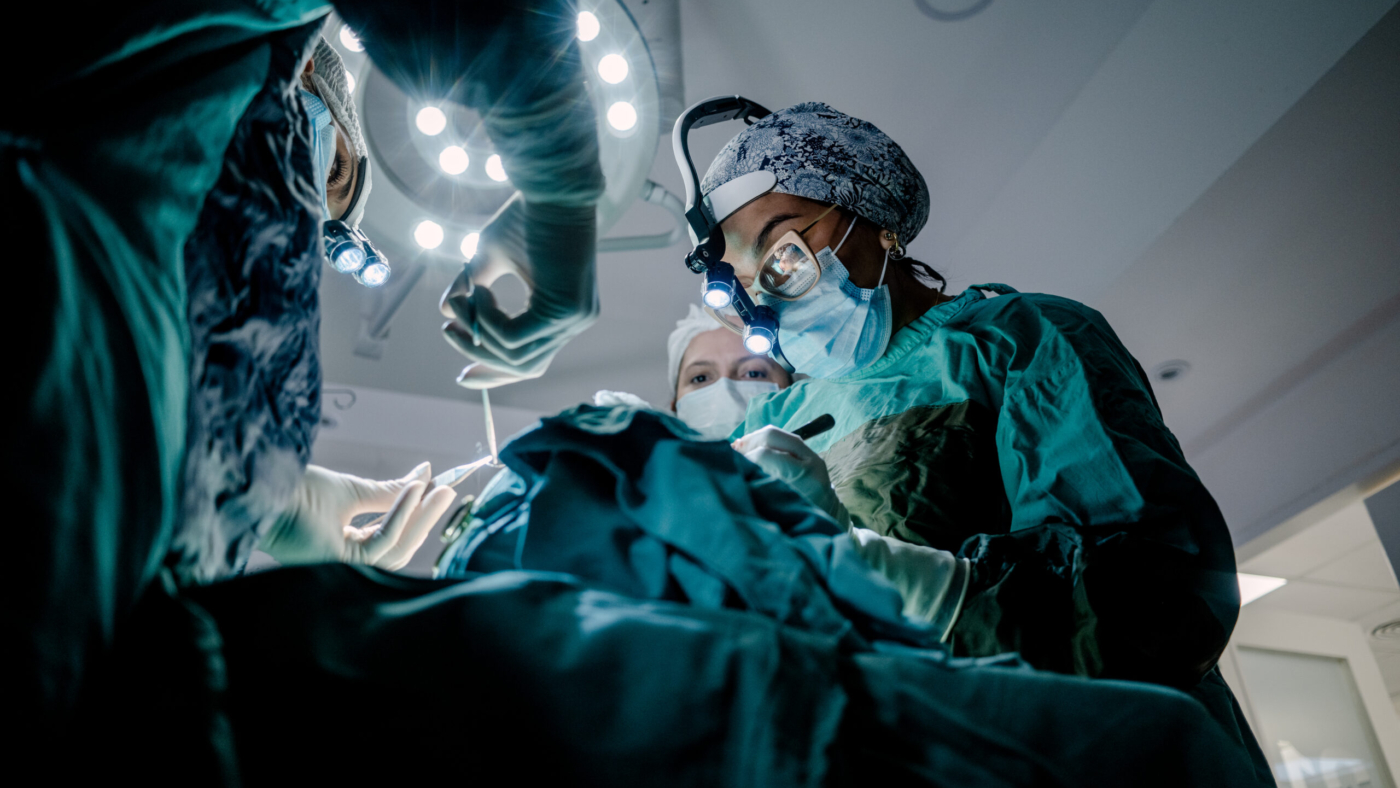 Two surgeons and an instrument technician in an operating room perform reconstructive surgery.