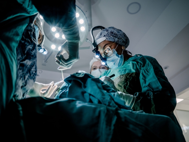 Two surgeons and an instrument technician in an operating room perform reconstructive surgery.